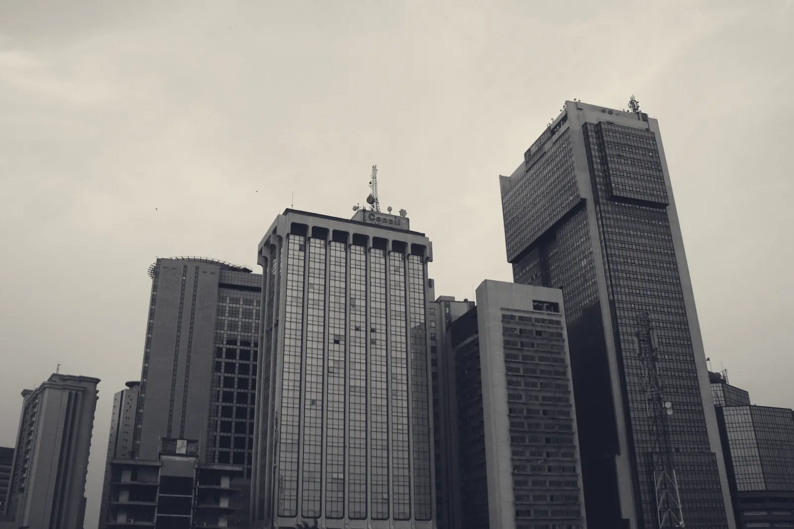 Looking up at a cluster of high-rise office towers on Lagos Island against a pale, hazy sky.